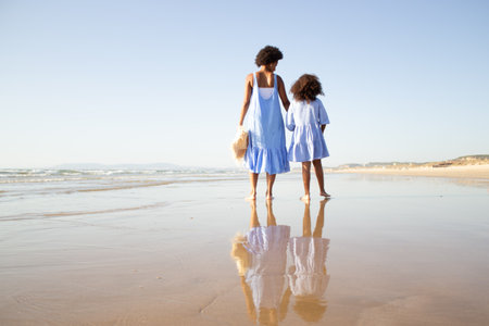 Back view of African American family walking on beach. Mother and daughter with dark curly hair spending time together on open air. Leisure, family time, togetherness conceptの写真素材