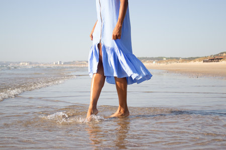 Close-up of womans bare feet. Woman walking at beach with a waves edge foaming gently beneath. Vacation, happiness conceptの写真素材