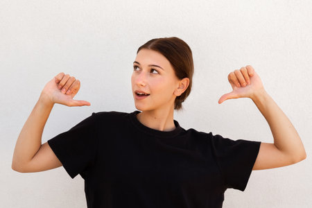 Portrait of happy young woman pointing thumbs at herself. Caucasian woman wearing black T-shirt...