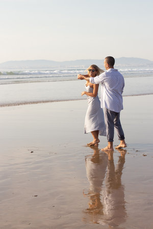 Lively male and female couple spending time at beach. Husband and wife in casual clothes hugging and dancing on summer day. Vacation, happiness, relationship conceptの写真素材
