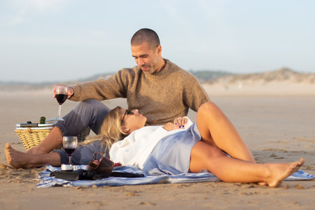 Tranquil couple at picnic at sunset. Top view of man and woman in casual clothes sitting and lying on blanket in rays of setting sun. Picnic, meal, love conceptの写真素材