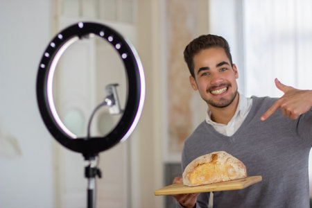 Portrait of bearded man holding loaf of bread on cutting board. Happy young man standing indoors...