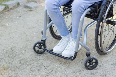 Person of unrecognizable age and gender sitting in wheelchair outdoors. Close-up shot of thin legs...