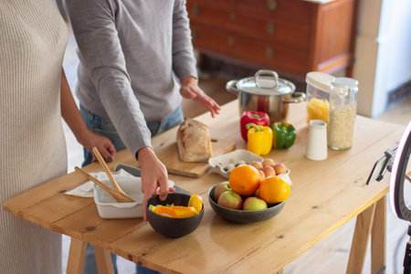 Close-up of table with fresh fruit and vegetables and human hands. View of small wooden table with products on it prepared by young couple for cooking meal. Healthy food and cooking together conceptの写真素材