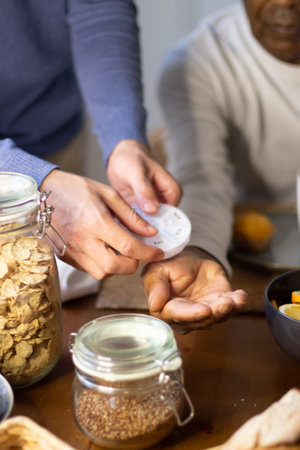Close-up of young mans hands giving medicine to granddad. Senior Latin man sitting at table with...