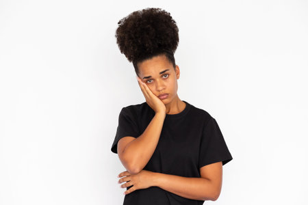 Portrait of unhappy young woman leaning head on hand against white background. African American...