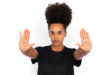 Portrait of serious young woman making stop gesture against white background. African American woman...