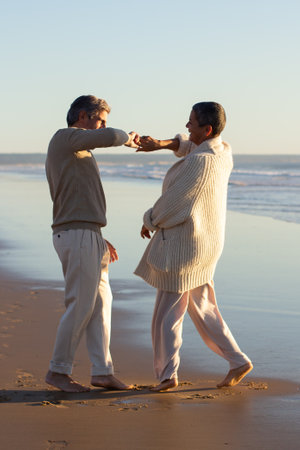 Romantic senior couple spending time at seashore at sunset, having fun and dancing barefoot on wet sand. Short-haired lady holding mans hand and laughing. Leisure, romance, relationship conceptの写真素材