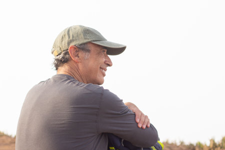 Back view of elderly man with backpack. Sporty man in casual clothes sitting, resting after hiking. Sport, adventure, rest conceptの写真素材