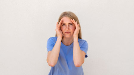 Attentive young woman trying to see something. Caucasian female model with blonde hair and blue eyes in casual clothes holding hands near her face trying to focus. Eyesight, concentration conceptの写真素材