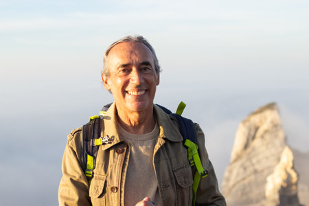 Portrait of elderly man at mountain peak. Sporty man in casual clothes looking at camera with smile....