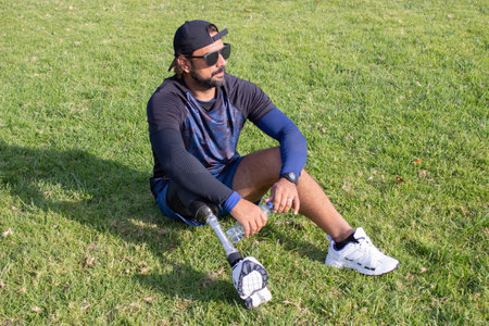 Tired man with prosthetic leg relaxing after training. Caucasian man with beard holding bottled...