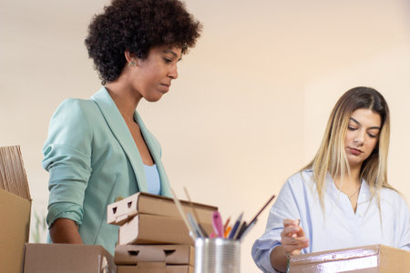 Serious postal employees working with packages. Caucasian girl taping cardboard box under control of supervisor in office. Postal service conceptの写真素材