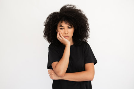 Displeased young woman holding hand on her cheek. Caucasian female model with afro hairstyle and...