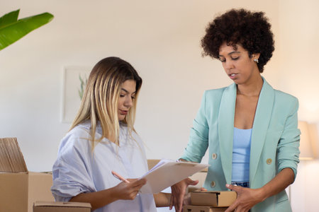 Postal coworkers examining numbers of parcels. Caucasian woman holding pen and clipboard while...