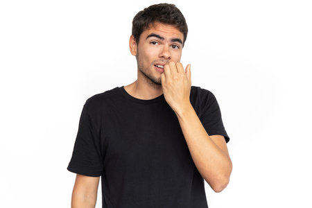 Confused young man biting nail. Portrait of nervous Caucasian male model with short dark hair in...