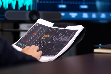 Close-up of printed stock market graphs. Corporate financier holding papers looking at market data...