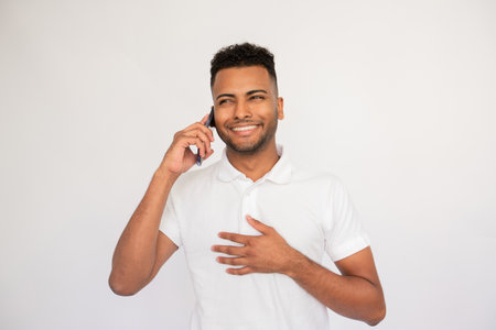 Satisfied young man talking on mobile phone. Male Indian model with brown eyes and curly hair in casual clothes speaking on phone with happy facial expression. Communication, modern technology conceptの写真素材