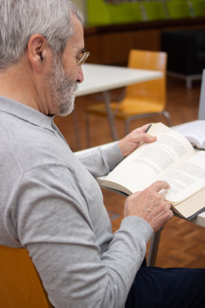 Side view of serious aged man reading books with pleasure. Relaxed grey-haired man focused on...
