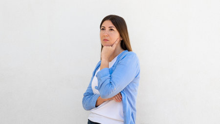 Portrait of pensive young woman posing with hand on chin over white background. Caucasian woman...