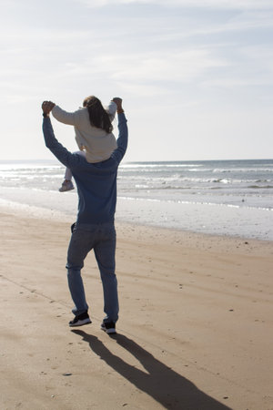 Back view of Japanese family walking on beach. Daughter riding on fathers back on sunny day. Leisure, vacation, parenting conceptの写真素材