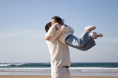 Happy father and daughter playing on beach. Japanese family walking, laughing, fooling around, lifting child up. Dad leisure, family time, parenting conceptの写真素材