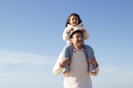 Happy Japanese family together on sunny day. Father and daughter playing, riding on shoulders. Leisure, family time, parenting conceptの写真素材