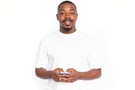 Joyful young man using smartphone. Male African American model with brown eyes, short haircut and...