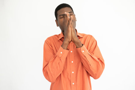 Portrait of tired young man rubbing nose over white background. Exhausted African American guy wearing orange shirt posing with closed eyes. Fatigue and stress conceptの写真素材