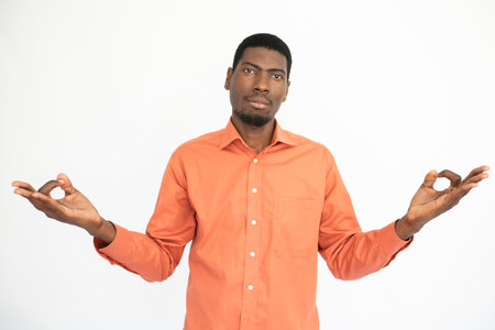 Portrait of confident young man making relaxation exercise. African American guy wearing orange shirt looking at camera and meditating. Balance and harmony conceptの写真素材