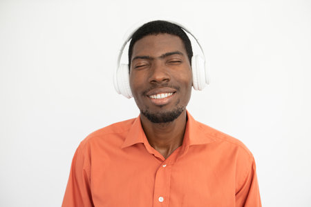 Portrait of happy young man enjoying music in headphones. African American guy wearing orange shirt listening to favorite songs. Music and leisure conceptの写真素材