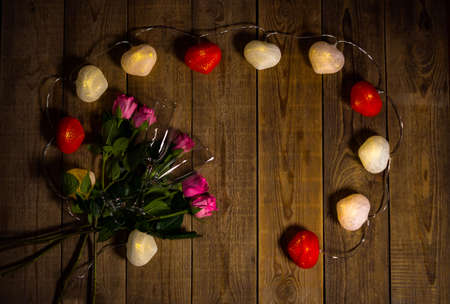 Still life with pink roses and heart shape garland lying on wooden surface filmed from above. Composition of flowers and wine glasses. Surprise for romantic date. Theme of Valentines Day celebration.の写真素材