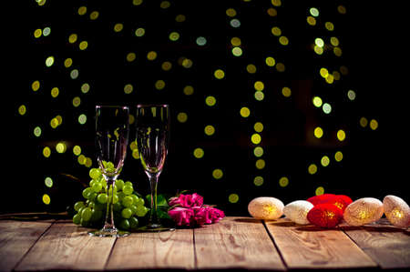 Romantic evening with flowers and fruit lying on the table next to couple of wine glasses. Still life of fruit and flashing lights. Surprise on Valentines Day. Theme of spending lovely date together.の写真素材