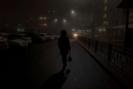 Night residential district with building and car parking covered by smog and silhouette of going man...
