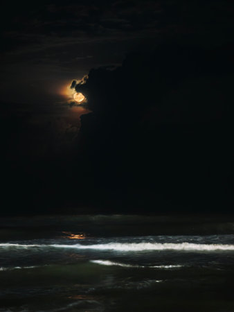 Bright moon above churning ocean creates reflective and mysterious nocturnal landscape