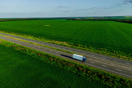 one blue truck on the higthway at sunset among the green fields with goods cargo delivery. seen from the air. Aerial view landscape. drone photography.の写真素材