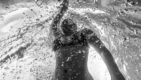 Black and white low angle underwater photography of a female swimmer gliding through bubbles in a...