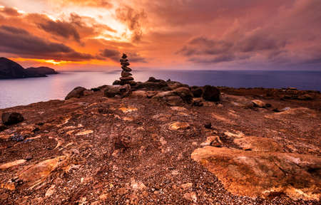 Beautifully colored sunrise over rocky coastline with heap of stones in the foreground, Madeira,...
