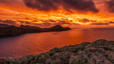 Seascape view of bay of water in between steep cliffs with reflection of beautifully colored sunrise on water surface, Madeira, Portugalの写真素材