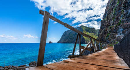 Seascape with wooden footbridge at the brim of a steep cliff against blue sky, Madeira, Portugalの写真素材
