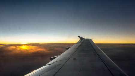 Aircraft lookout to airplane wing against cloudscape at sunset time