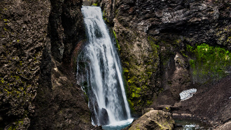 Mossy ravine with lttle waterfall inbetween volcanic rock formation, Iceland