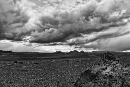 Black and white photo of moss and lichen covered rock of volcanic origin in an ash covered desert beneath dramatic sky with stormclouds, Icelandの写真素材