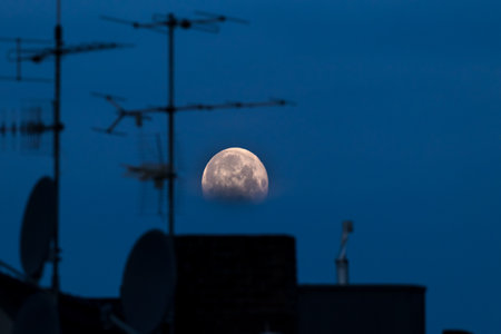 Full moon against black sky without stars above city roofs with tv antennaeの写真素材
