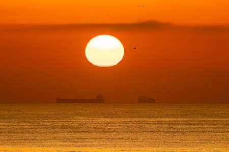 A big ball sun setting on a calm Mediterranean sea with container ship
