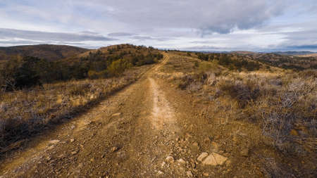 Driver point of view of dirt road on barren mountain ridge under overcast sky