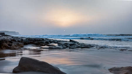 Misty humid sunset over sand beach with scattered rock at Atlantic ocean, Western Sahara, Morocco