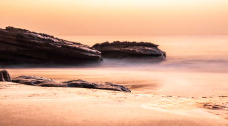 sunset over swirl patterns of waves rolling onto rocky coastline, Atlantic ocean, Morocco