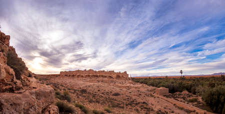 landscape with damaged medieval kasbah ksar ruin agsinst blue sky with white clouds, Morocco