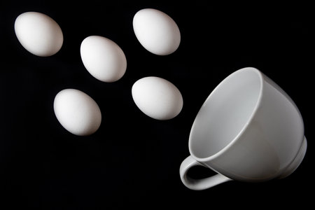 White chicken eggs and a big white cup over black backgroundの写真素材